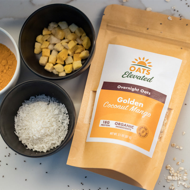 Oats Elevated Golden Coconut Mango overnight oats package surrounded by its fresh ingredients, including coconut, dried mango, and turmeric.