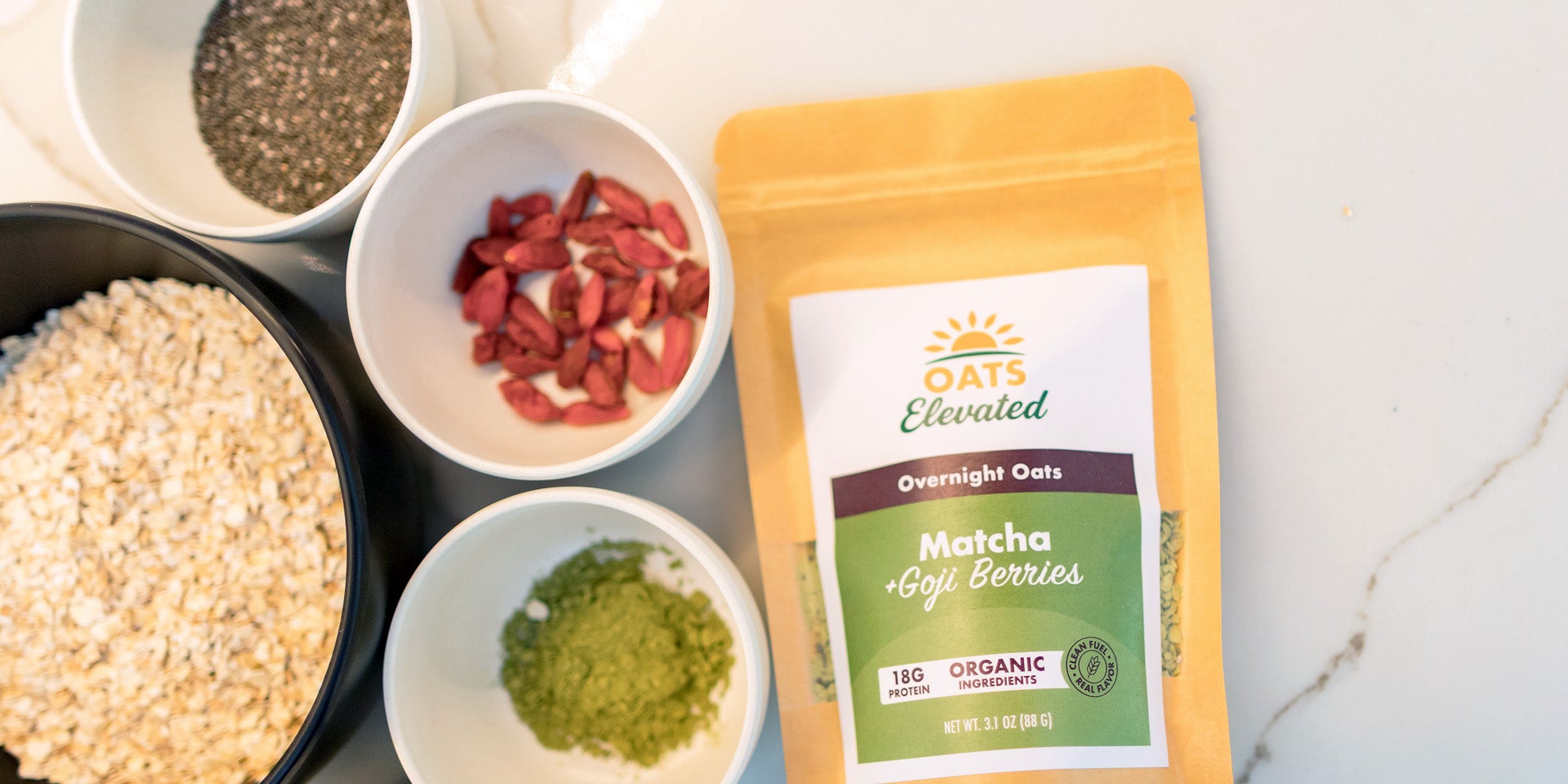 Overhead view of Oats Elevated Matcha plus Goji Berries overnight oats, surrounded by bowls of its raw, organic ingredients.