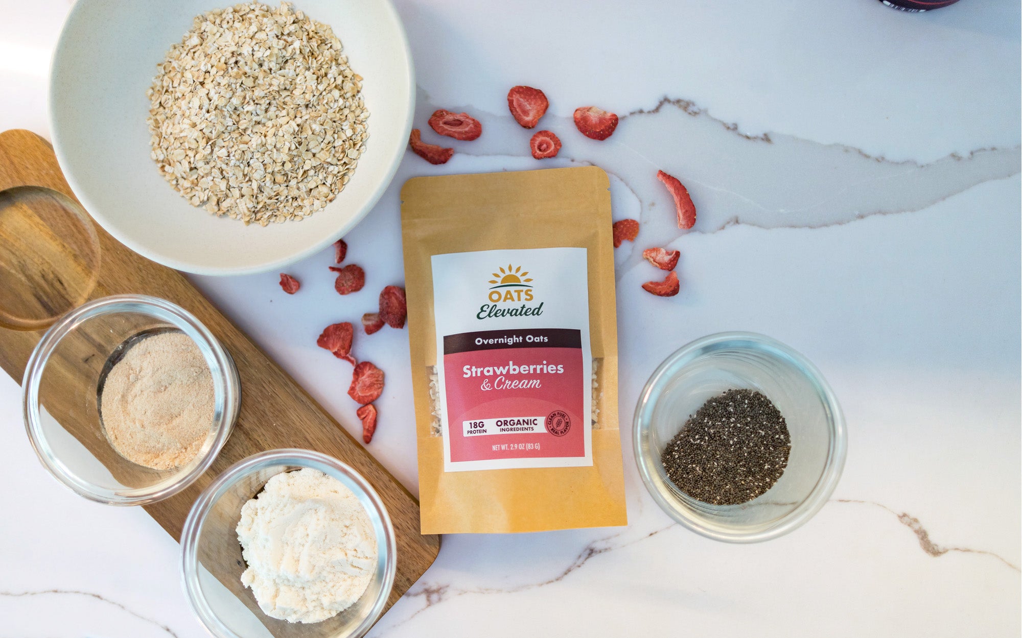 Oats Elevated Strawberries and Cream overnight oats package surrounded by its raw ingredients.
